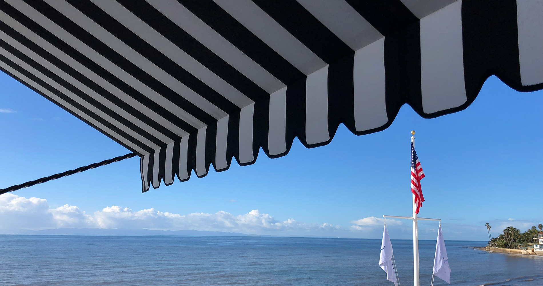 Striped awning above ocean with three shoreline flags.