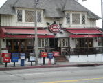 Restaurant with sign reading The Cock, newspaper racks, and mailbox out front.