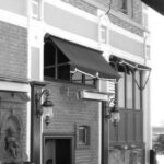 Building exterior with awning, vintage lamps, and small statue.
