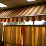 Striped awning above large windows with closed curtains.