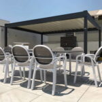 Plastic chairs and tables arranged under a pergola on patio.