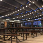 Wooden picnic tables under string lights at pizza counter.