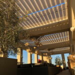 Outdoor lounge with pergola, sofas, hanging lights, and plants.
