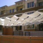 Fabric shades arranged in waves over pergola structure.