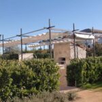 Pergola with fabric canopy over stone barbecue grill.