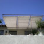 Second-floor balcony with metal railing, potted plants, fabric canopy.