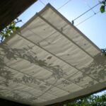 Fabric shade shows leaf shadows above wooden frame.