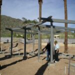 Two people under a steel frame structure under construction.