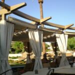 Pergola patio with draped curtains and tables in a garden.