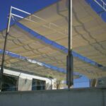 Fabric shade sails stretched across metal frame above building.