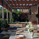 Long table set for dining under wavy pergola.