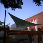 Triangular shade sail over fenced outdoor area.