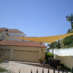 Two-car garage with shade sail overhead and trash bins nearby.