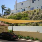 Car parked in driveway under a large shade sail.