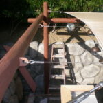 Canopy supported by beams and cables over stone wall.