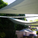 Rectangular shade sails above backyard patio with furniture.
