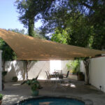 Triangular shade sail above patio furniture and small pool.