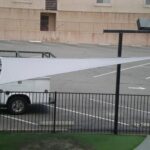 Triangular shade sail attached to metal frame and fence.