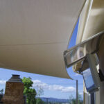 Large shade sail over patio with wall-mounted TV and chimney.